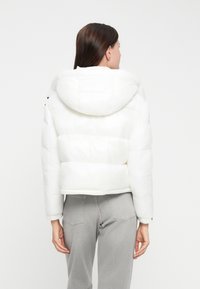 White puffer jacket with a hood, cropped design, quilted texture, and elastic cuffs, paired with gray high-waisted jeans.