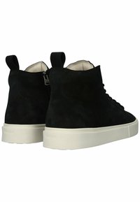 Zapatillas de ante negras de caña alta con suela de goma blanca, que cuentan con cierre de cordones, cremallera lateral y tiradores en el talón.