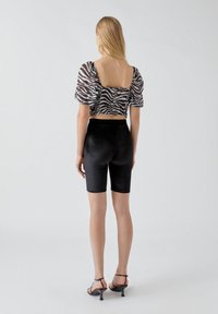 Shorts de vélo en velours noir associés à un haut court noir et blanc à manches bouffantes imprimé zèbre, vu de dos.