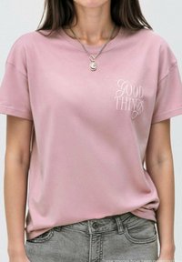 Růžové bavlněné tričko s krátkým rukávem a volným střihem, s nápisem "DOBRÉ VĚCI" tištěným světle kurzívou na levé části hrudi.