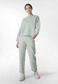 Sudadera verde claro y pantalones a juego hechos de una tela suave; ajuste relajado, puños acanalados y dobladillos de pantalón enrollados. El calzado presenta acentos verdes.