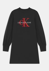 Svart bomullsklänning med långa, puffiga ärmar. Framsidan visar en röd och vit broderad logotyp: "CALVIN KLEIN JEANS" med stiliserad "CK."