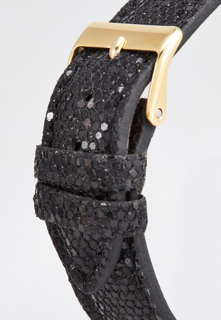 Bracelet de montre noir avec une surface texturée ornée de sequins, fermé par une boucle en métal doré. Dos en cuir lisse, matériel minimal.