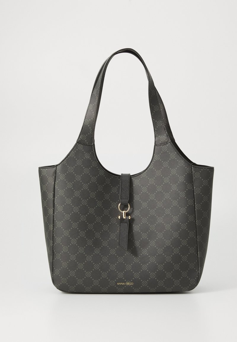 Sac fourre-tout noir avec motif circulaire subtil, une bandoulière, anneau doré central et détail de fermoir, et logo « Anna Field » en bas au centre.