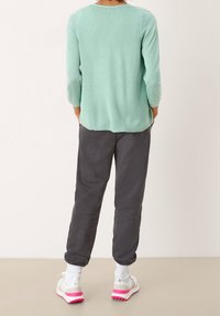 Ljusgrön stickad tröja med trekvartslånga ärmar, tillsammans med mörkgrå mjukisbyxor och vita sneakers med rosa sulor.