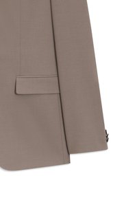 Μανίκι καφέ σακακιού και κάτω μέρος κορμού που δείχνουν τσέπη με καπάκι και τέσσερα μαύρα κουμπιά στη μανσέτα.