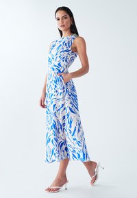 Sleeveless midi dress in white with a blue abstract pattern, featuring a fitted bodice, side pockets, and a decorative accent on one shoulder.