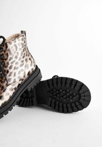 Botas hasta el tobillo con estampado de leopardo y acabado brillante, cordones negros y suela de goma texturizada con un patrón de tracción.