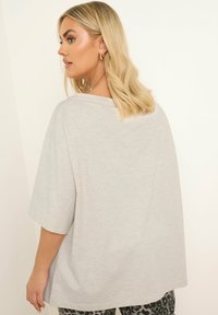 Camiseta gris claro de gran tamaño con mangas cortas y un escote amplio, hecha de una tela suave, con una textura lisa y un ajuste casual.