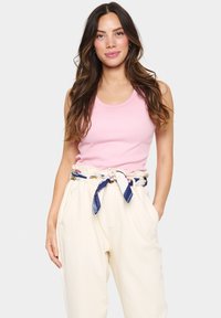 Svjetloružičasta rebrasta majica bez rukava u kombinaciji s kremasto obojenim, širokim hlačama, dodatno ukrašena remenom s uzorkom u mornarsko plavim prugama.