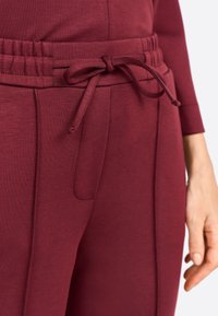 Pantalons de survêtement bordeaux avec une taille élastique à cordon de serrage, poches latérales et texture de tissu lisse et douce.