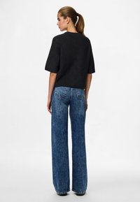 Svart strikket kortermet topp kombinert med høytlivs vidbukser i blå jeans. Jeansene har en falmet vask og strukturerte baklommer.