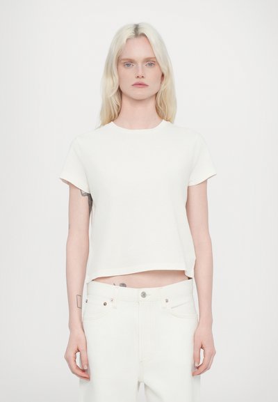 White cropped t-shirt made of soft cotton with short sleeves and a round neckline. Paired with high-waisted white jeans.