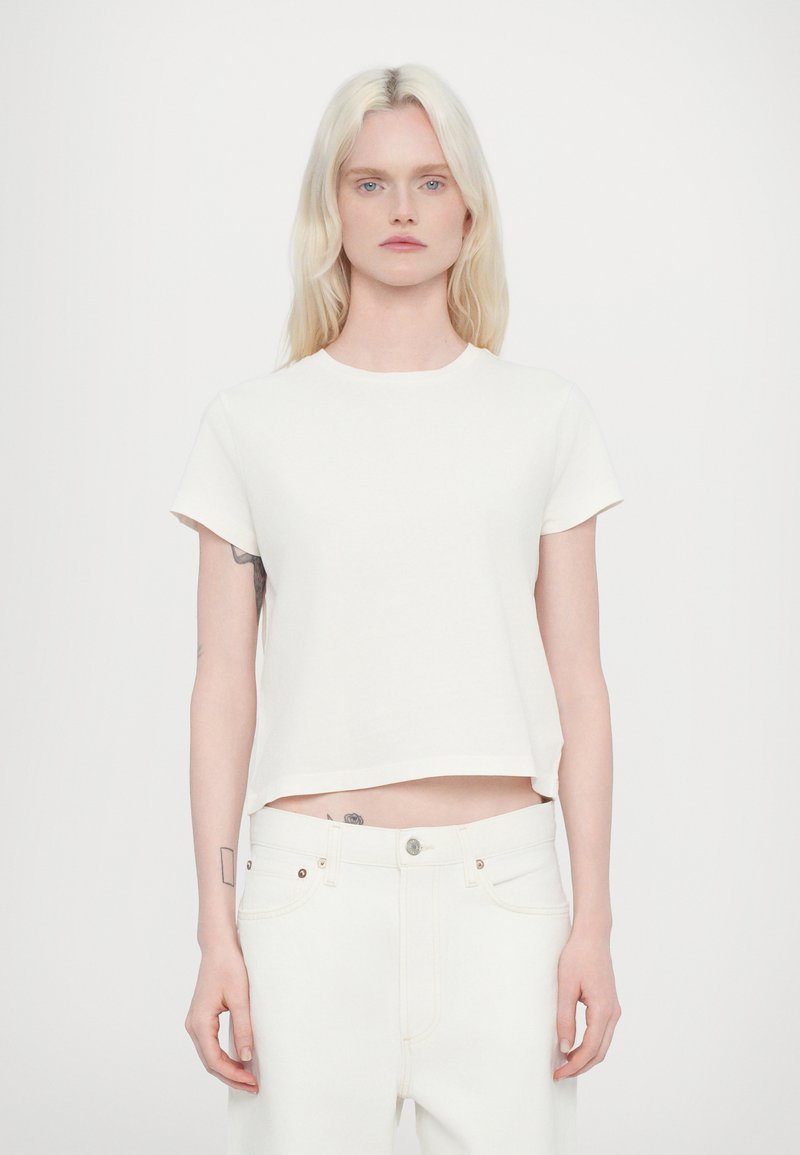 T-shirt blanc court en coton doux avec des manches courtes et un col rond. Associé à un pantalon en jean blanc taille haute.