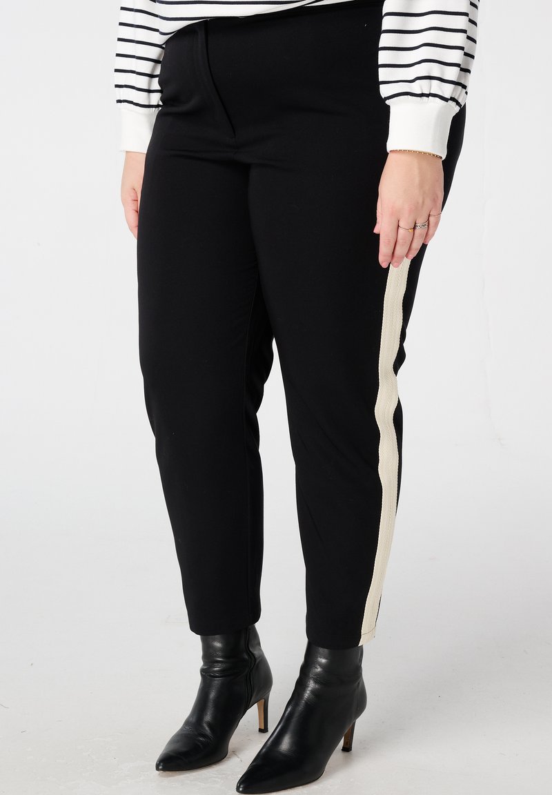 Zwarte aangesloten broek met een crème-zijstreep, gemaakt van rekbaar materiaal. Gecombineerd met zwarte pumps met een puntige neus.