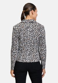 Luipaardprint blazer in wit, crème en browntinten. Heeft een kraag, lange mouwen en een getailleerde pasvorm. Gecombineerd met zwarte broek.