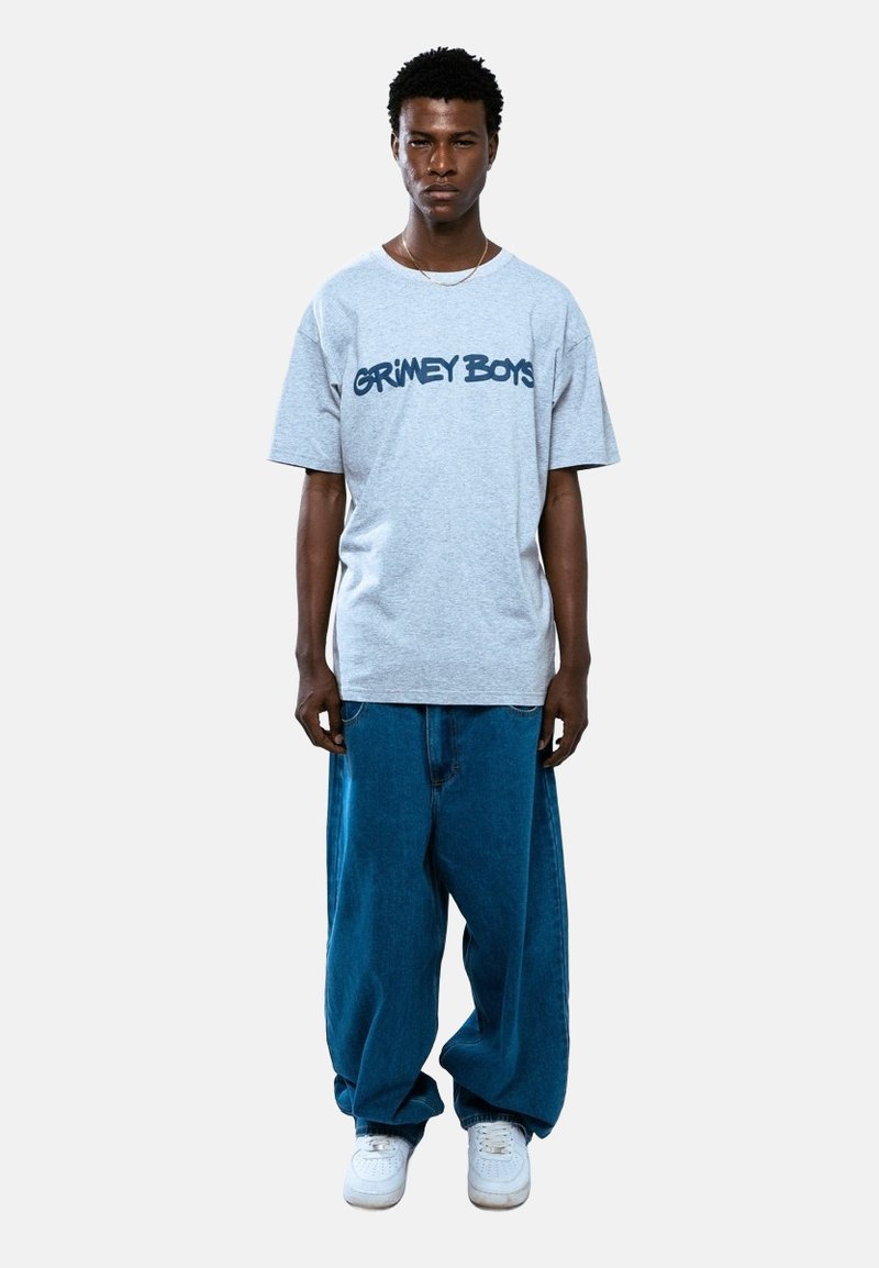 Szary t-shirt z krótkim rękawem z napisem "GRIMEY BOYS" w granatowym kolorze, zestawiony z luźnymi niebieskimi dżinsami i białymi trampkami.