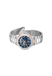 Silverfärgad klocka i rostfritt stål med blå urtavla, transparent mekanism och detaljer i roséguld. Har ett länkarmband och framträdande markeringar.