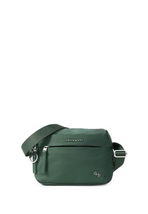 Sac bandoulière vert foncé avec sangle réglable, poche avant zippée et logo Hedgren en métal sur une surface en tissu lisse.