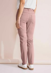 Růžové slim-fit kalhoty s hladkým povrchem, dvěma zadními kapsami a středním pasem, doplněné bílými teniskami. Neutrální pozadí.