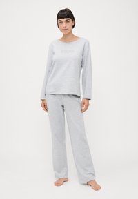 Lys grå loungewear-sett laget av myk bomull. Langermet topp med rund hals og brodert logo. Matchende bukser med løs passform.