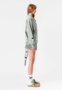 Chaqueta de gran tamaño a rayas grises con pantalones cortos plisados a juego, que presenta una etiqueta en la manga y un lazo decorativo en la parte posterior. Combinada con zapatos marrones.