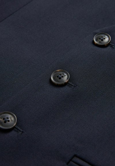 Marineblazer av tyg med fyra runda, mörka knappar med två hål vardera, sydda på en slät, texturerad yta.