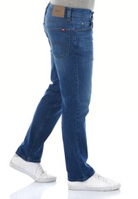 Jeans de mezclilla azul con corte recto, que cuentan con una parche de cuero en la cinturilla, dos bolsillos traseros y detalles de costura sutiles.