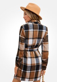 Abito a quadri marrone con maniche lunghe, vita con cintura e colletto. Il motivo presenta accentuazioni bianche e nere, con un tessuto morbido e texturizzato.