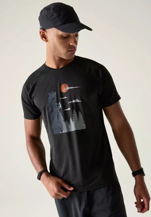 Hombre con gorra negra y camiseta negra con gráfico de escalador en roca, árboles, sol naranja y nubes, mirando hacia abajo hacia un lado.