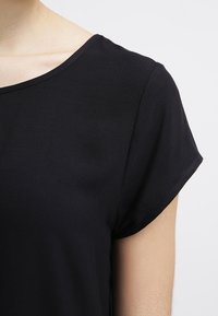 Musta lyhythihainen kangastoppi, jossa on pyöreä kaula-aukko ja sileä pinta. Vaate on rento mitoitukseltaan ja siinä on siistit saumat reunoilla.