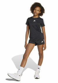 Set di t-shirt sportiva nera e pantaloni corti, con accenti bianchi a tre strisce, realizzato in tessuto leggero, abbinato a scarpe da ginnastica bianche e calzini.