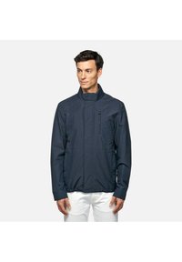 Marineblauwe jas met een staande kraag, een rits aan de voorkant, zijzakken en een borstzak. Gladde textuur, lichtgewicht materiaal.