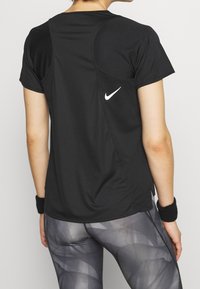 Svart atletisk t-shirt med korta ärmar, med en böjd design på axlarna och en vit Nike-logga på ryggen. Bärs med mönstrade grå tights.