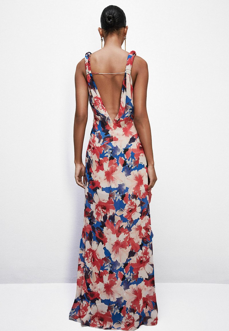 Donna con i capelli raccolti a bun, che indossa un vestito floreale lungo fino al pavimento, senza maniche, con una profonda scollatura a V sul retro e una sottile tracolla sopra la schiena.