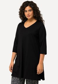 Schwarzes V-Ausschnitt-Tunika-Oberteil mit Dreiviertelärmeln, aus weichem Stoff, bietet einen lockeren Schnitt. Kombiniert mit gemusterten grauen Leggings.