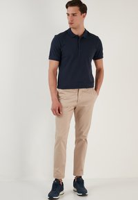 Polo de marina con mangas cortas, combinado con chinos beige claro y zapatillas navy, con un cuello clásico y cierre de dos botones.