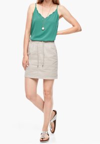 Top verde senza maniche con bordi scalloppati, abbinato a una mini gonna beige chiaro con vita elasticizzata e cordoncino. Sandali argentati.