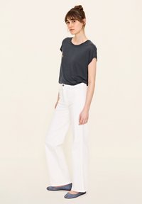 Schwarzes T-Shirt mit kurzen Ärmeln, weiße weite Hose und blaue flache Schuhe. Textil mit Struktur und lockerer Passform. Einfaches Design, keine auffälligen Muster.