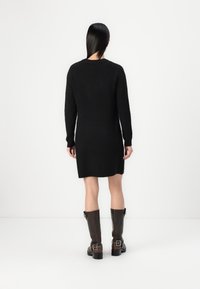 Vestido de suéter negro de punto con mangas largas, textura acanalada y longitud hasta el muslo, combinado con botas de cuero marrón hasta la rodilla.