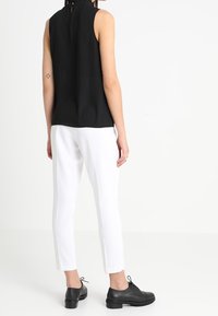 Svart ärmlös topp med nyckelhålsrygg, kombinerad med slim-fit vita byxor och svarta snörskor. Slät struktur, minimalistisk design.