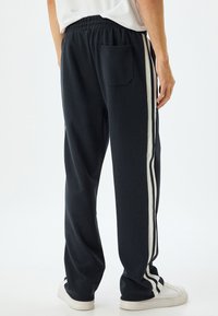 Sorte sweatpants med hvide sidelister, som har et elastisk taljebånd og en baglomme. Lavet af blødt, fleksibelt stof.