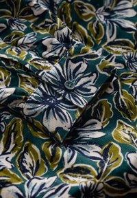 Blommönstrad tyg med en färgsättning i grönt, marinblått och vitt. Texturen är ribbad; har en knappad manschett med en matchande knapp.