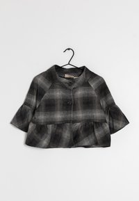 Svart och grå rutigt kort jacka med volang nederkant, trekvartslång ärm och två stora framknappar som hänger på en svart galge.