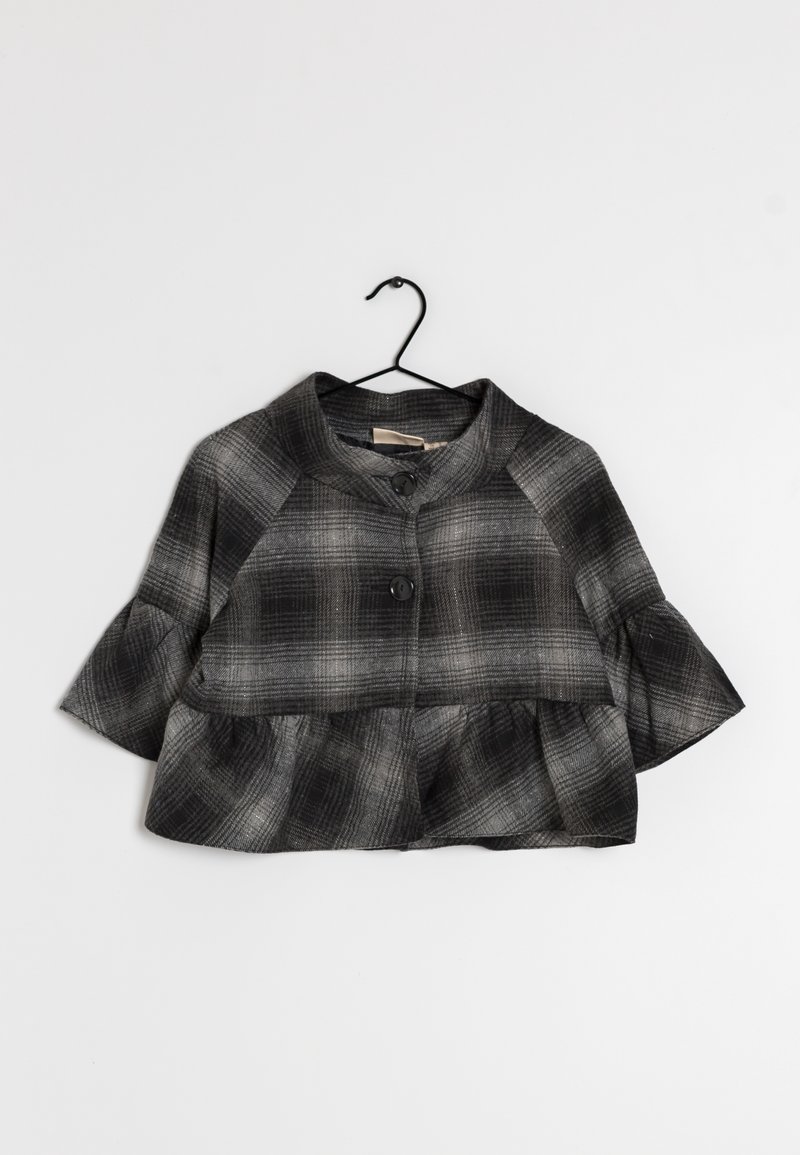 Svart och grå rutigt kort jacka med volang nederkant, trekvartslång ärm och två stora framknappar som hänger på en svart galge.