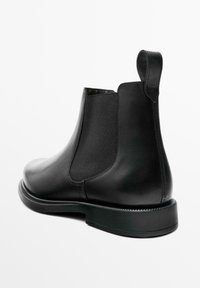 Botte Chelsea en cuir noir avec panneaux latéraux élastiques, languette de tirage à l'arrière, finition lisse avec bout arrondi et semelle en caoutchouc plate.