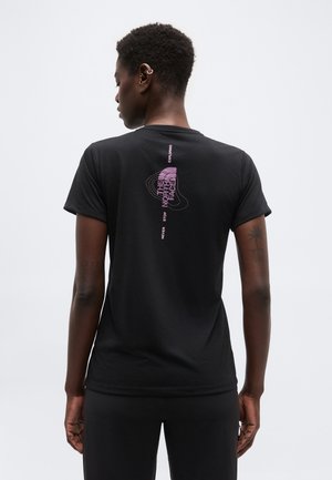 Νεαρό άτομο με κοντά, σγουρά μαλλιά, ντυμένο με μαύρο T-shirt που έχει ροζ κείμενο "The North Face" και περιγραμμικές γραμμές στην πλάτη.