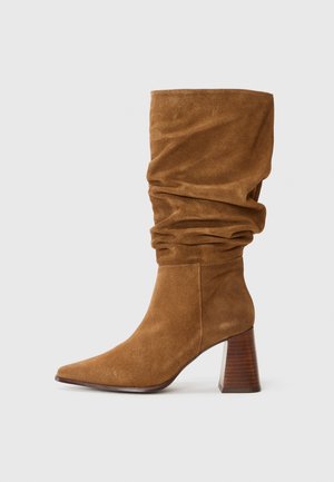 Brown suede boot with a slouchy design, pointed toe, and a textured wooden block heel. Features soft material and smooth stitching details.
