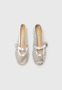 Scarpe Mary Jane argento con rete trasparente decorata con borchie rotonde argentate e cinturini con fibbia, posizionate su uno sfondo bianco.