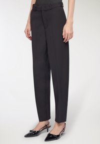 Czarne eleganckie spodnie z wysokim stanem i z paskiem, proste nogawki oraz subtelna tekstura. W zestawieniu z czarnymi lakierowanymi szpilkami z odkrytymi piętami.